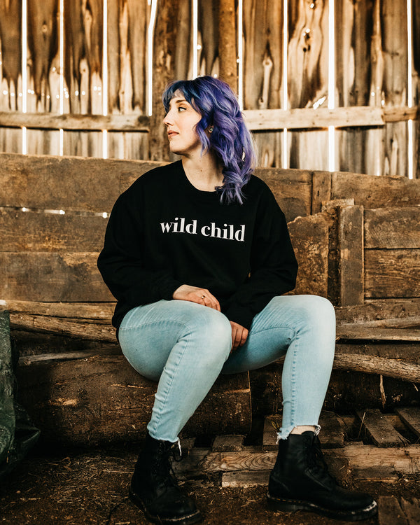 woman sitting in barn wearing black sweater and jeans 