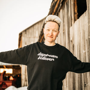 woman standing outside wearing daydream believer unisex sweatshirt 